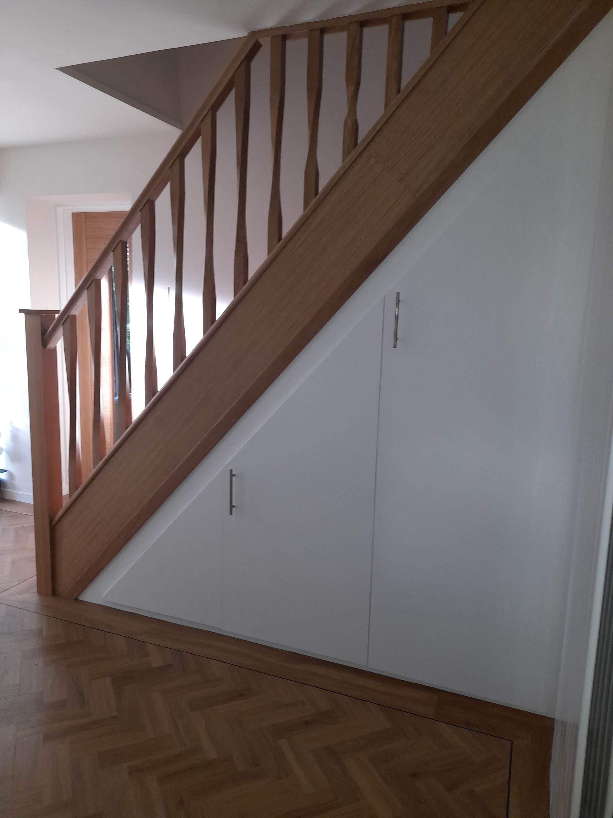 The finished staircase with full-height under stair cupboards and a herringbone floor