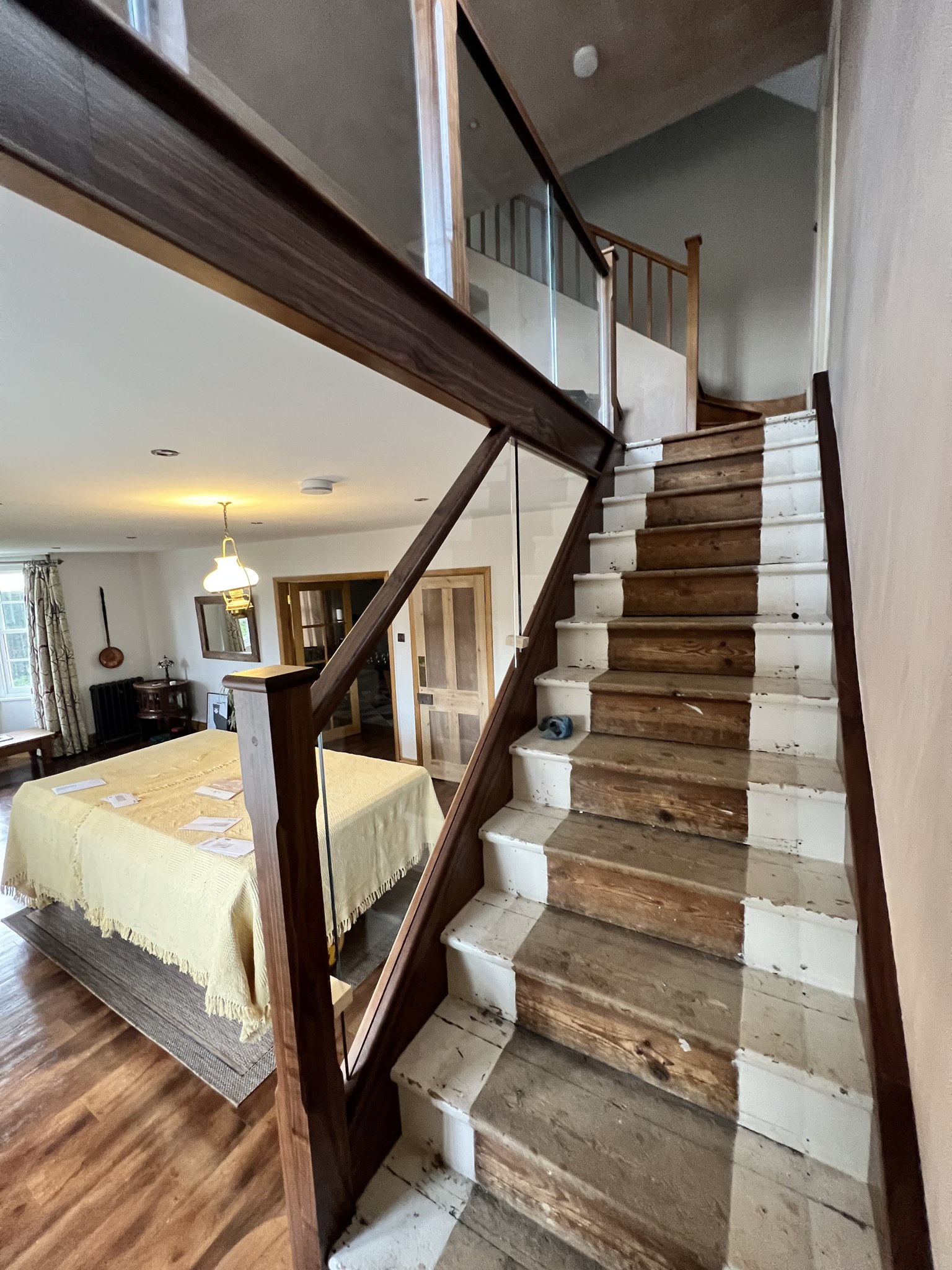 A staircase mid-renovation: stripped treads with a new dark timber handrail and glass